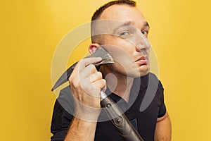 One young brutal man, firefighter shaving with an axe over yellow studio background.