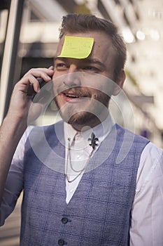 One young businessman, talking on a phone, with sticky note glued to his forehead