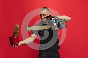 One young caucasian man with cactus and electric saw posing over red background.