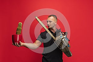 One young caucasian man with cactus and electric saw posing over red background.