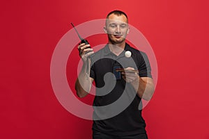 One young caucasian man with ping pong racket and walkie-talkie playing table tennis over red background.