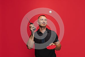 One young caucasian man with ping pong racket and walkie-talkie playing table tennis over red background.
