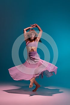 One young flexible contemp dancer in lilac dress dancing  on gradient blue white background in neon.