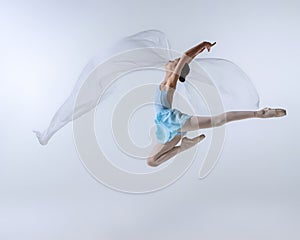 One young girl, aspiring ballerina in blue dress and pointes dancing with cloth  on gray background. Art, grace