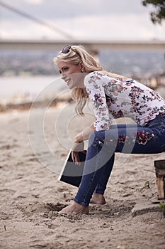 One young girl, sitting on steps on beach sand, summer, happy smiling, holding a book outdoors. side view