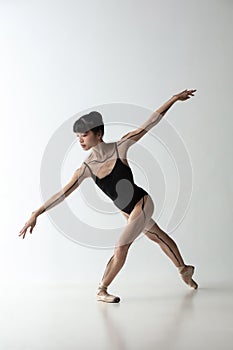 One young and graceful ballerina dancing  on light gray studio background. Art, motion, action, flexibility