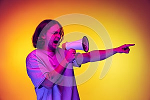 One young handsome man in white t-shirt shouting at megaphone  on orange background in neon light. Concept of