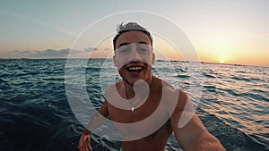 One young happy man enjoying and having fun alone at the beach in the water jumping looking at the camera while taking a selfie