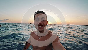 One young happy man enjoying and having fun alone at the beach in the water jumping looking at the camera while taking a selfie