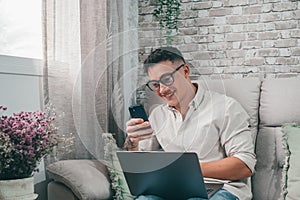 One young happy man surfing the net using his laptop at home sitting on the sofa enjoying free time and relaxing alone.