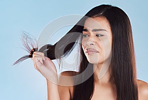 One young hispanic woman looking unhappy and worried about her unhealthy hair while posing against a blue studio