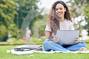 One young hispanic woman working on her laptop while sitting outside on an open field. A beautiful mixed race female