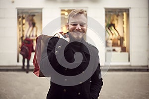 One young man, 20-29 years, looking to camera in front, upper body shot. Smiling holding shopping bag on his back