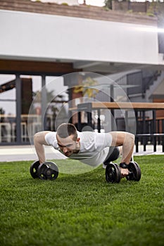 One young man, 20-29 years old, doing push ups with weights in a beautiful backyard of a fancy house