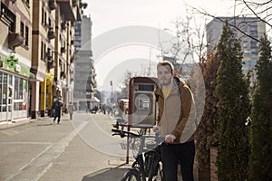 One young man, 20-29 years old, pushing his bicycle on a street in city. pedestrians in background