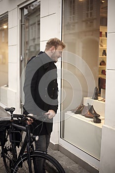 One young man, 20-29 years old, shopping for fancy shoes. standing in front of a store with his bicycle, looking to a window shop