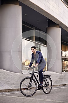 One young man, 20-29 years old, wearing suit, looking smiling. riding, pedaling standing, fancy bicycle. full length body. modern
