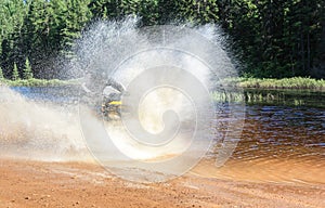 Man driving motocross ATV quad through splashing river lake water with high speed. Foy, Foyross Lake, Sudbury, Canada.