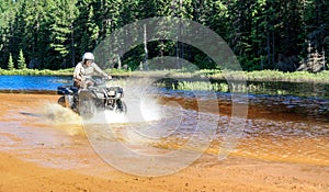 Man driving motocross ATV quad through splashing river lake water with high speed. Foy, Foyross Lake, Sudbury, Canada.