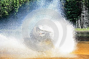 Man driving motocross ATV quad through splashing river lake water with high speed. Foy, Foyross Lake, Sudbury, Canada.