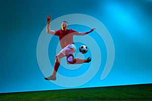 One young man, professional soccer football player training over soccer field background in neon light. Copy space for