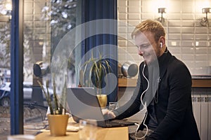 One young man, sitting in coffee shop, drinking from cup working on laptop