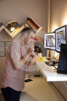 One young man, thinking in his room. looking to write something on a post-it note. in front of a standing desk, and computer