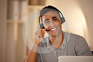 One young man wearing headset and working on a laptop in an office at night. Happy guy doing freelance work as a call