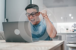 One young man working and winning something with laptop at home. Happy and euphoric teenager celebrating good news and having fun