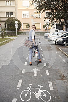 One young man, 20-29 years old, wearing hipster suit, smart casual, looking back to camera, rear view. in city on bike track