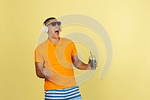 One young smiling handsome asian man in bright summer clothes with headphones isolated over yellow studio background.