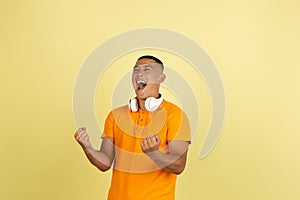 One young smiling handsome asian man in bright summer clothes with headphones isolated over yellow studio background.