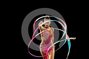 One young sportive girl, rhythmic gymnastics artist performing with ribbon isolated on dark background. Concept of sport