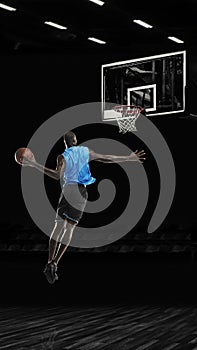 One young sportsman basketball player training in gym, idoors isolated on dark background. Concept of sport, game