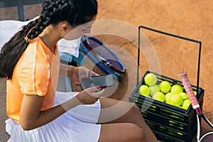 One young sportswoman, professional tennis player with phone on tennis court in bright summer day.