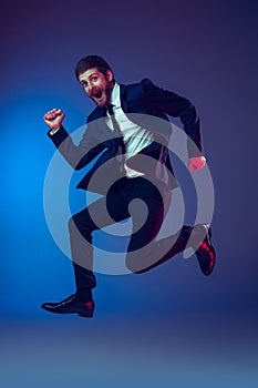 One young stylish man in business suit jumping isolated on dark blue studio background. Concept of human emotions