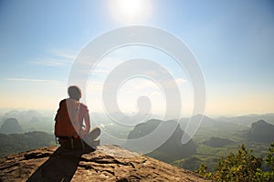 young traveler with backpack sit on the mountain peak rock observing locality photo