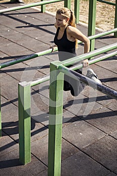 One young woman, 20-29 years, exercising outdoors in public park, outdoor gym, doing pull ups, push up,