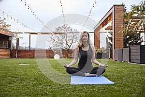 One young woman,20-29 years old, doing yoga while sitting in a sukhasana pose in a beautiful backyard