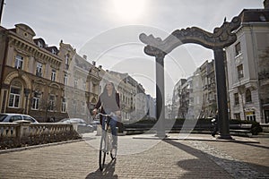 One young woman, 20-29 years old, riding a retro old bicycle on a old city European square. Smiling, happy