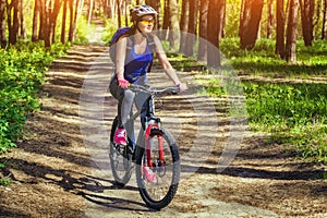 One young woman - an athlete in a helmet riding a mountain bike outside the city, on the road in a pine forest