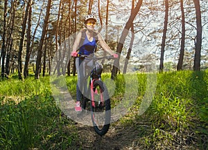 One young woman - an athlete in a helmet riding a mountain bike outside the city, on the road in a pine forest