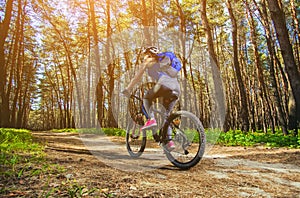 One young woman - an athlete in a helmet riding a mountain bike outside the city, on the road in a pine forest