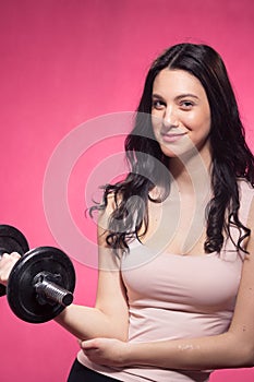 One young woman, dumbbell weights holding, pink background