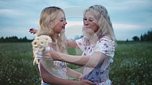 One young woman gives her girlfriend a bouquet of daisies in the field and they hug