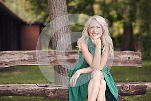 One young woman portrait, sitting in wood bench, green dress, 25 years old, smiling happy, looking to camera.