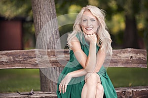 One young woman portrait, sitting in wood bench, green dress, 25 years old, smiling happy, looking to camera.