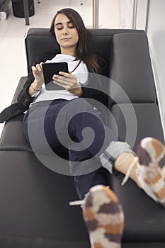 One young woman, white-collar worker, relaxing on sofa, working on tablet in modern office indoors