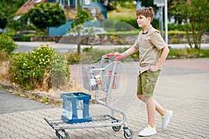 onfident School Boy Pushes the Shopping Cart Through a Bustling Supermarket. Handsome Teenager Gathers Groceries and