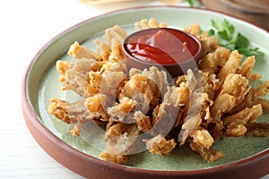 Onion blossom with ketchup served on white wooden table, closeup